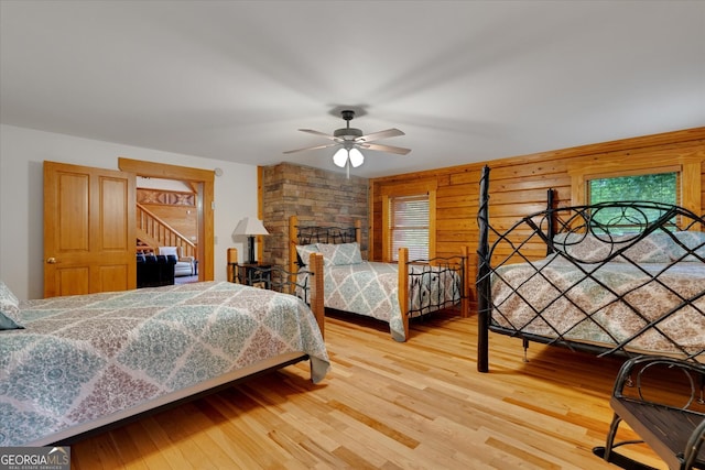 bedroom with light wood-type flooring, wood walls, and ceiling fan