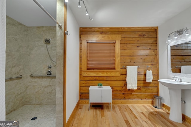 bathroom with wood walls, rail lighting, a tile shower, wood-type flooring, and sink