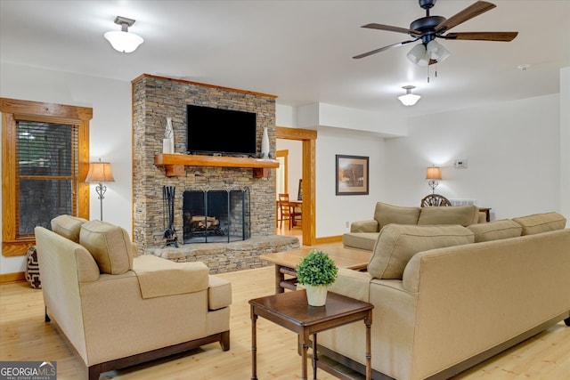 living room featuring wood-type flooring, a stone fireplace, and ceiling fan