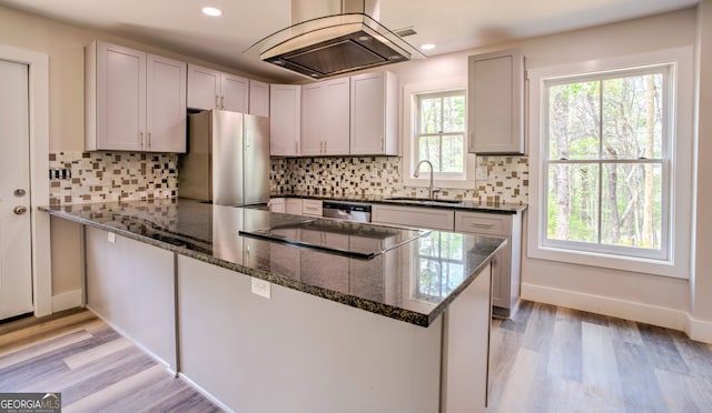 kitchen featuring island range hood, stainless steel appliances, light hardwood / wood-style flooring, dark stone counters, and sink