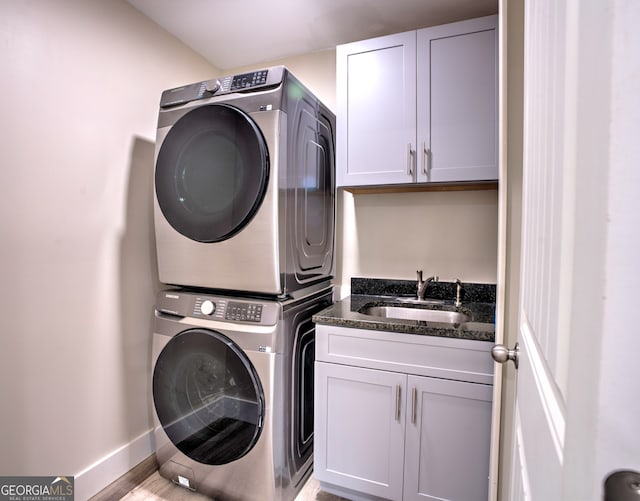 laundry area with cabinets, light hardwood / wood-style floors, stacked washer / drying machine, and sink