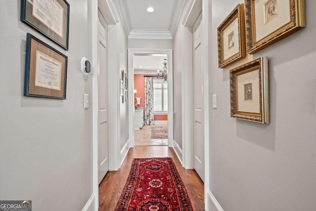 hallway featuring wood-type flooring, ornamental molding, and a notable chandelier