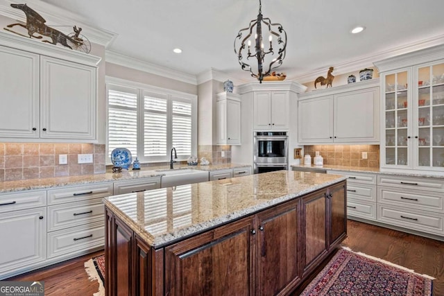 kitchen with decorative light fixtures, backsplash, double oven, white cabinets, and sink