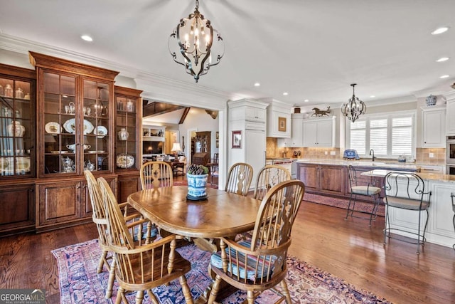 dining space with dark wood-type flooring, a notable chandelier, crown molding, and sink