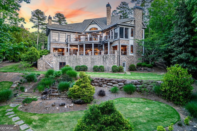 rear view of property featuring a balcony, stairs, a yard, stone siding, and a chimney