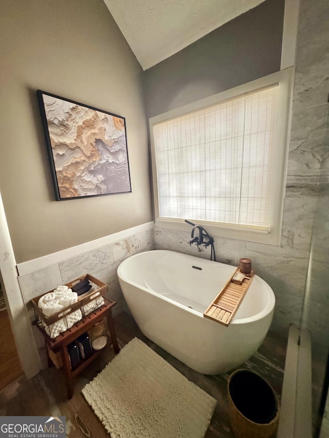 bathroom featuring tile walls, hardwood / wood-style floors, lofted ceiling, and a tub