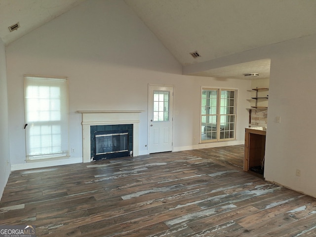 unfurnished living room featuring dark wood-type flooring, a tiled fireplace, and high vaulted ceiling