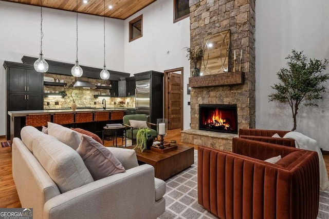 living room with a stone fireplace, light hardwood / wood-style flooring, wooden ceiling, and a high ceiling