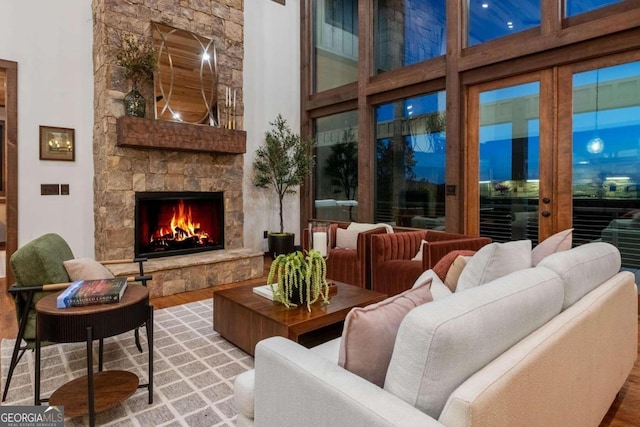 living room featuring french doors, a stone fireplace, hardwood / wood-style floors, and a high ceiling