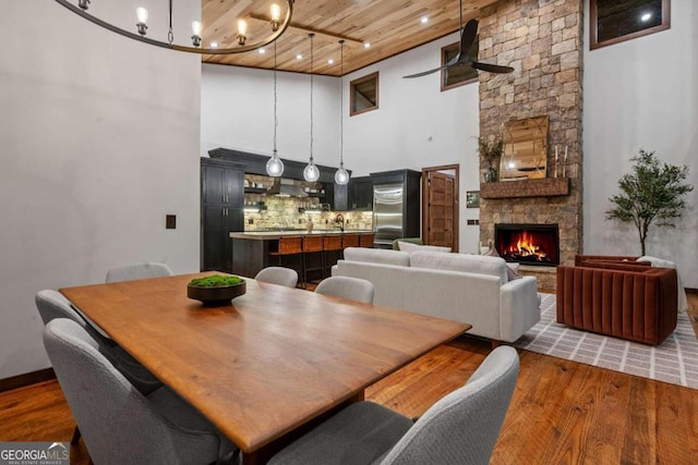 dining area with a fireplace, ceiling fan with notable chandelier, hardwood / wood-style floors, a towering ceiling, and wood ceiling