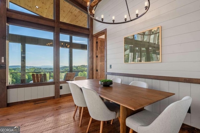 dining space with hardwood / wood-style flooring, an inviting chandelier, wooden walls, and vaulted ceiling