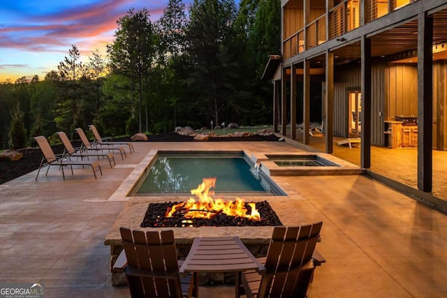 pool at dusk with a patio, an outdoor fire pit, and an in ground hot tub