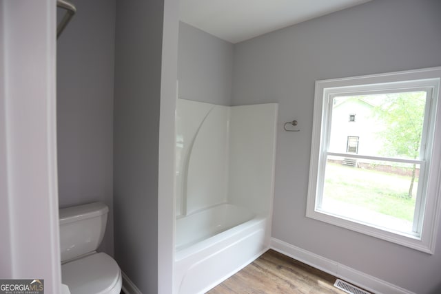 bathroom featuring toilet, shower / bathing tub combination, hardwood / wood-style floors, and plenty of natural light