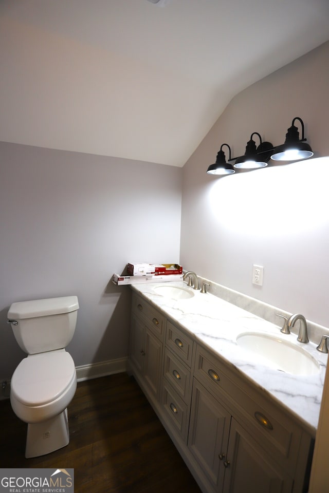 bathroom with dual vanity, toilet, hardwood / wood-style floors, and vaulted ceiling