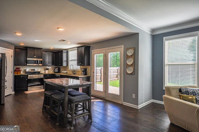 kitchen featuring a kitchen breakfast bar, dark hardwood / wood-style flooring, backsplash, appliances with stainless steel finishes, and light stone counters