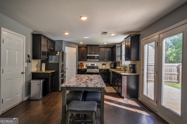 kitchen featuring appliances with stainless steel finishes, a kitchen island, tasteful backsplash, light stone counters, and dark hardwood / wood-style flooring