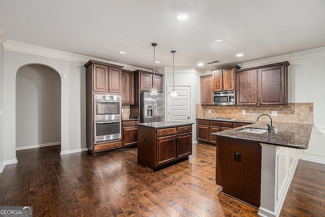 kitchen with hanging light fixtures, decorative backsplash, a center island with sink, appliances with stainless steel finishes, and ornamental molding