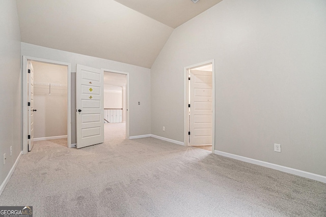 unfurnished bedroom with a walk in closet, light colored carpet, vaulted ceiling, and a closet