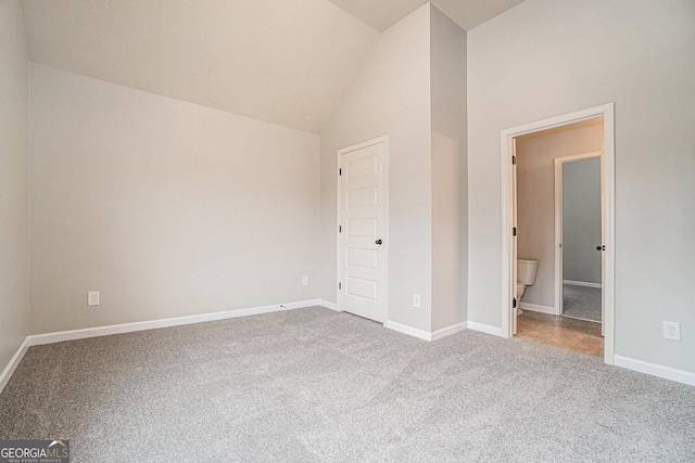 unfurnished bedroom featuring carpet floors, high vaulted ceiling, and ensuite bath