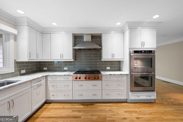 kitchen featuring wall chimney exhaust hood, white cabinets, tasteful backsplash, light wood-type flooring, and stainless steel appliances