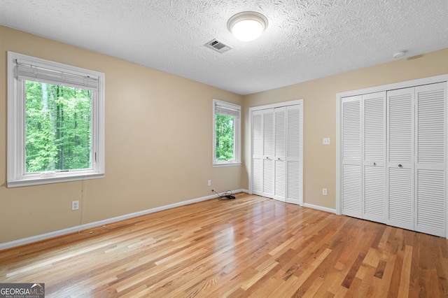 unfurnished bedroom featuring light hardwood / wood-style floors, two closets, and a textured ceiling