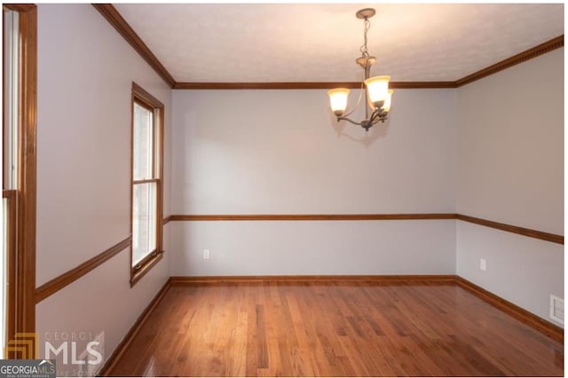 empty room with wood-type flooring, crown molding, and an inviting chandelier