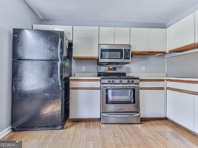 kitchen featuring a textured ceiling, stainless steel appliances, light wood-type flooring, and white cabinetry