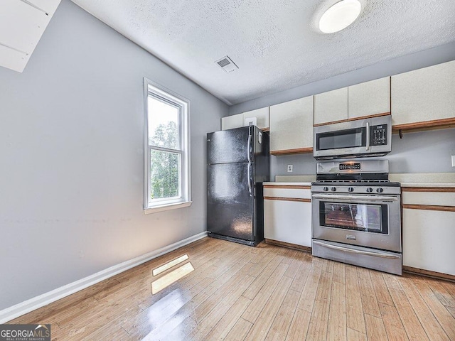 kitchen featuring white cabinets, a textured ceiling, stainless steel appliances, and light hardwood / wood-style floors