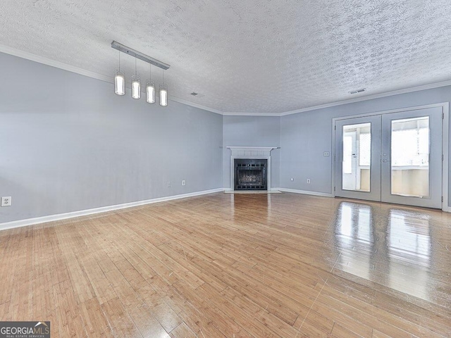 unfurnished living room with a textured ceiling, french doors, light wood-type flooring, and ornamental molding