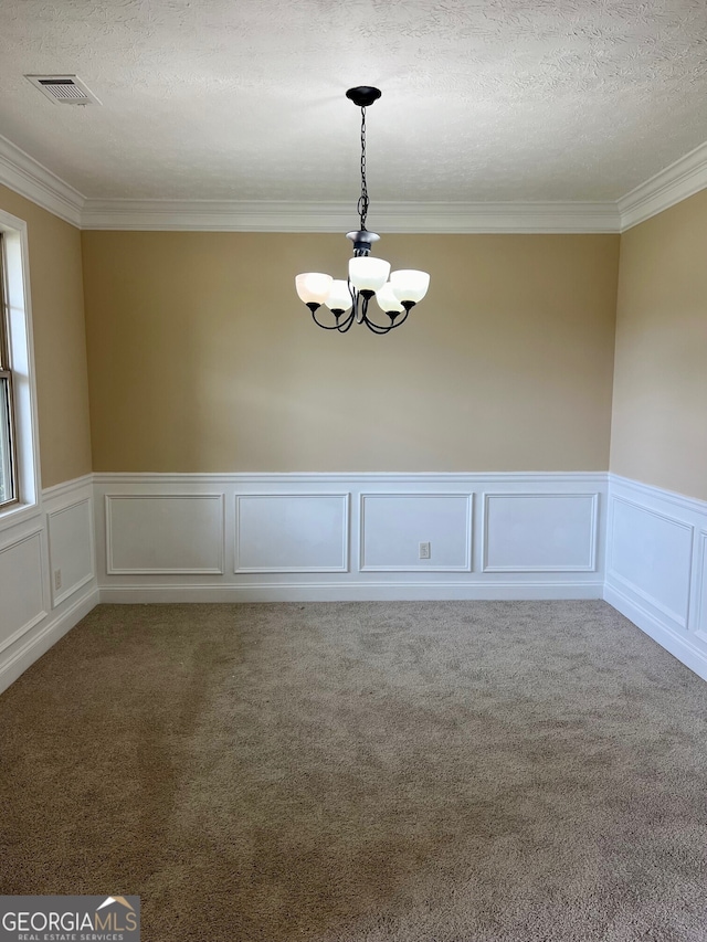 spare room with a textured ceiling, carpet floors, a notable chandelier, and ornamental molding