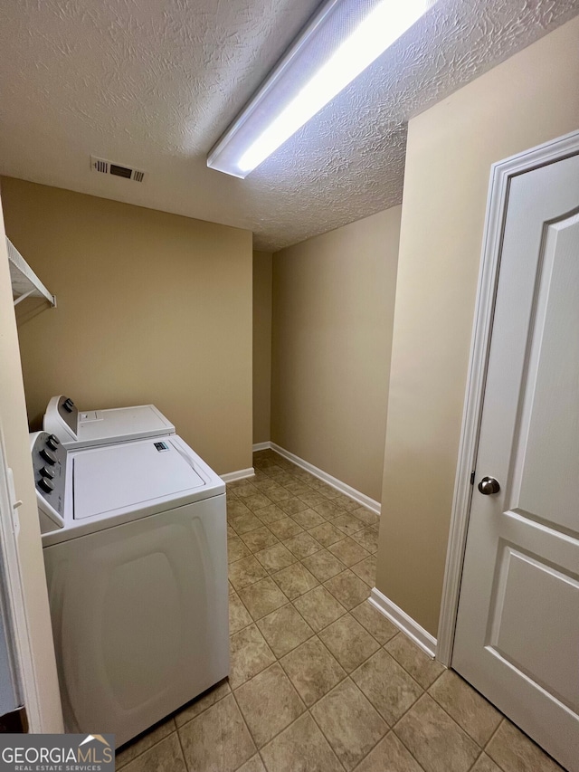 washroom with a textured ceiling, independent washer and dryer, and light tile floors