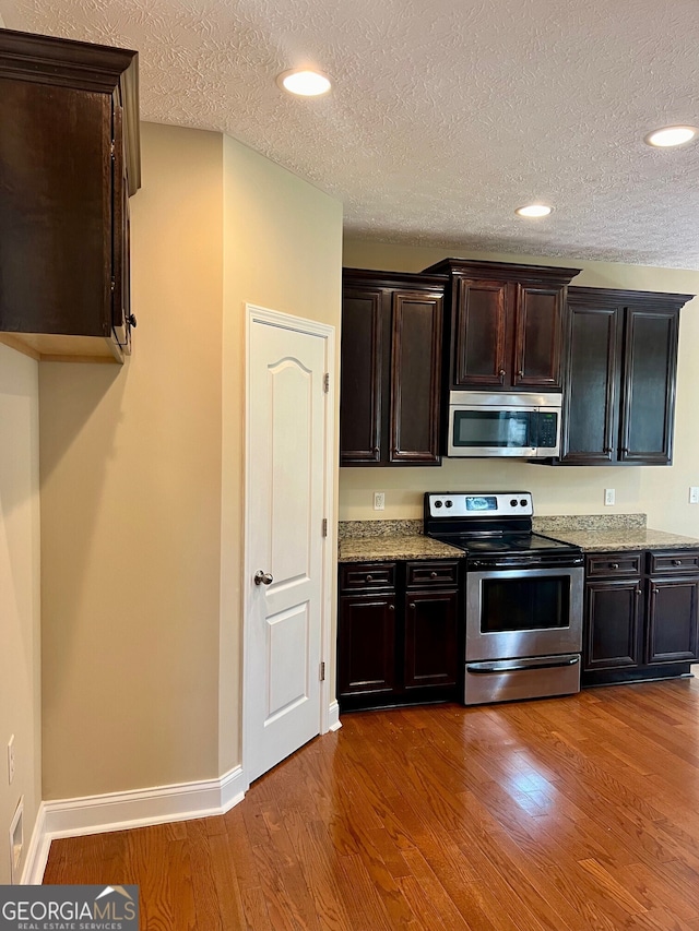 kitchen featuring hardwood / wood-style flooring, appliances with stainless steel finishes, a textured ceiling, and light stone counters