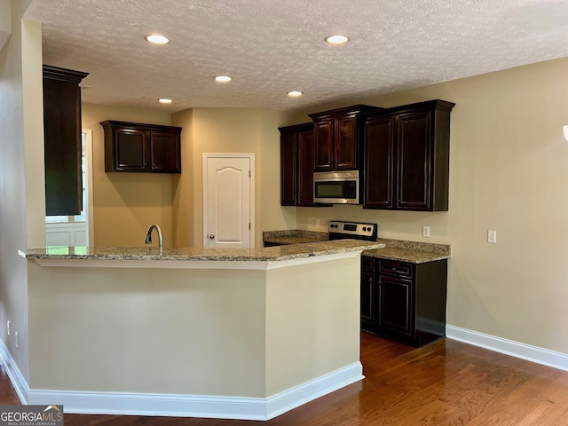 kitchen featuring wood-type flooring, a textured ceiling, dark brown cabinets, and light stone counters