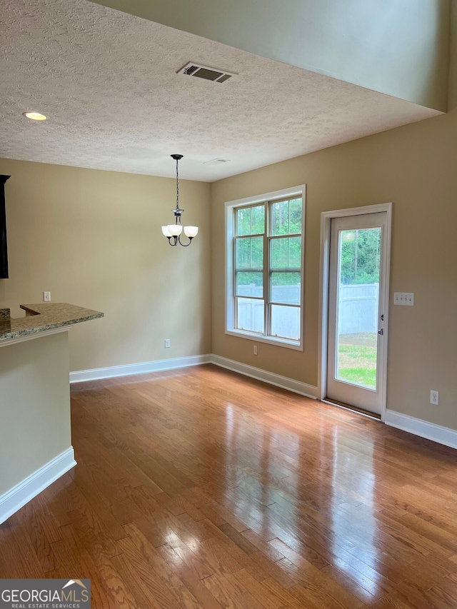 unfurnished room featuring a textured ceiling, an inviting chandelier, and hardwood / wood-style flooring