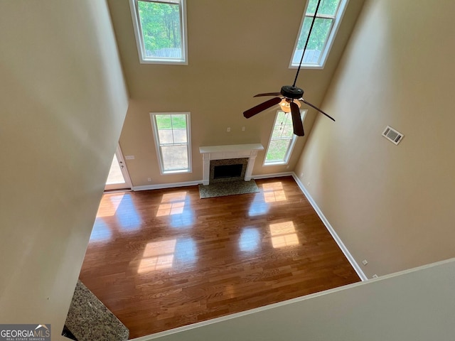 unfurnished living room featuring ceiling fan, a fireplace, hardwood / wood-style floors, and a towering ceiling