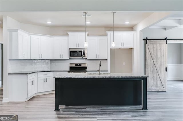 kitchen with a center island with sink, light hardwood / wood-style flooring, range, a barn door, and sink