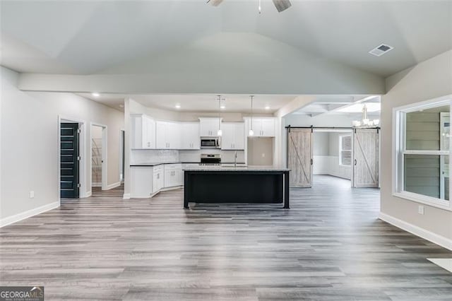 kitchen with an island with sink, a barn door, hardwood / wood-style floors, and white cabinets