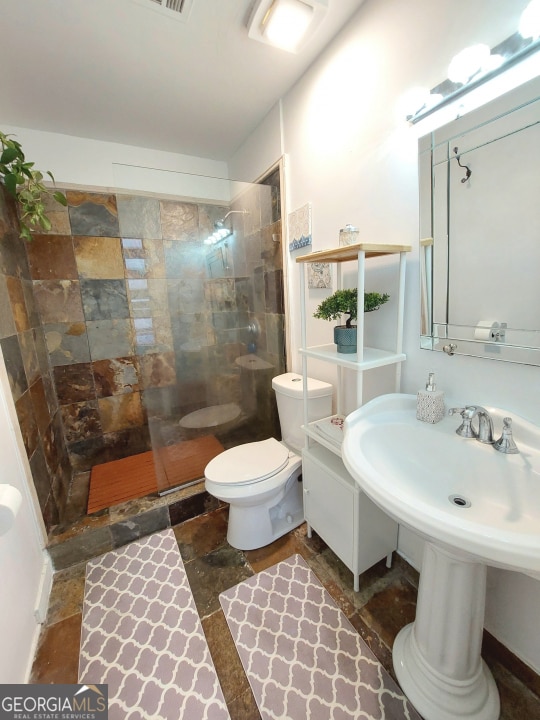 bathroom featuring a shower with door, tile flooring, and toilet