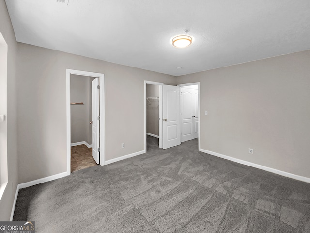 unfurnished bedroom with a spacious closet, a closet, and dark carpet