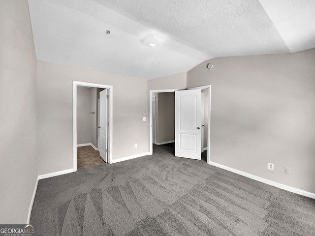 unfurnished bedroom with dark carpet, a textured ceiling, and lofted ceiling