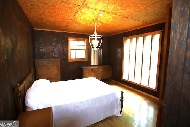 bedroom featuring wooden walls, hardwood / wood-style floors, and a chandelier