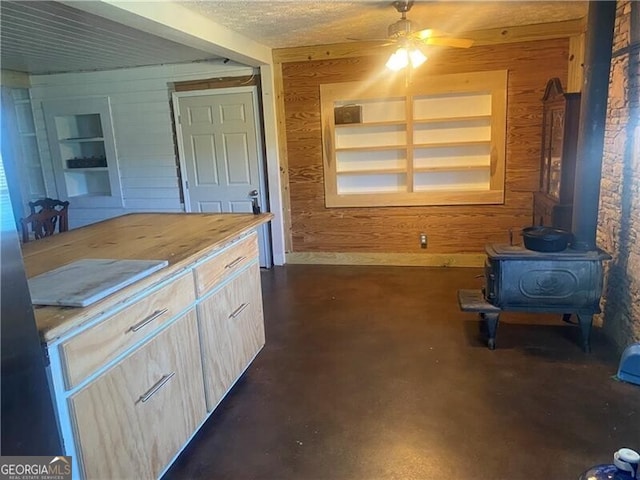 kitchen with wooden walls, a wood stove, built in shelves, ceiling fan, and a textured ceiling