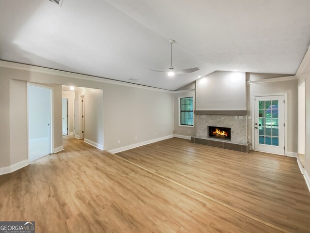 unfurnished living room featuring ceiling fan, light wood-type flooring, a tiled fireplace, lofted ceiling, and ornamental molding