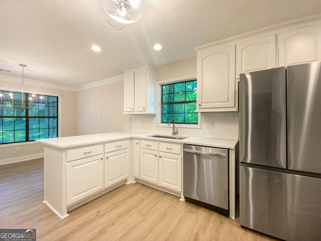 kitchen with decorative light fixtures, white cabinets, light wood-type flooring, stainless steel appliances, and sink