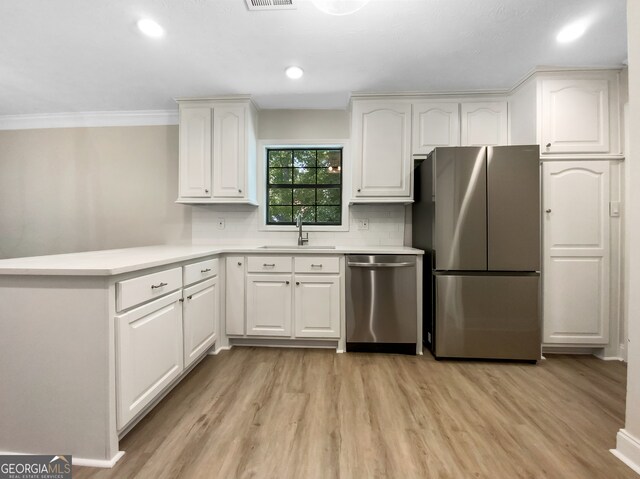 kitchen with white cabinetry, ornamental molding, stainless steel appliances, sink, and light hardwood / wood-style floors