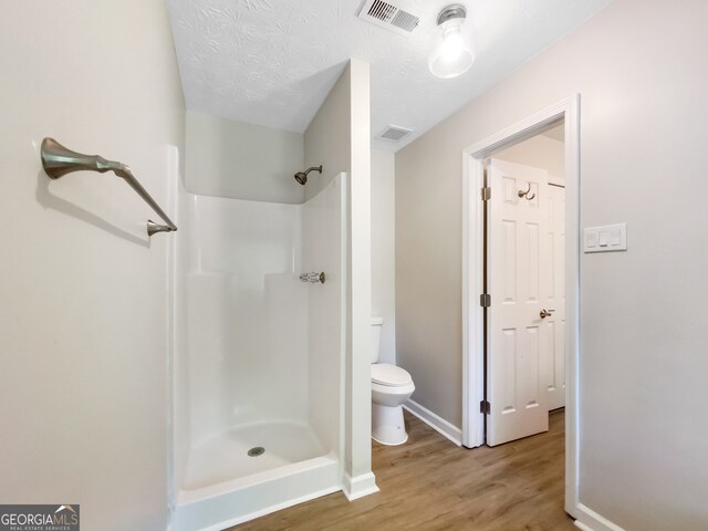 bathroom with wood-type flooring, a textured ceiling, toilet, and walk in shower