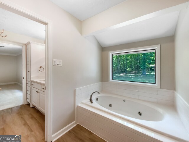 bathroom featuring wood-type flooring, vaulted ceiling, vanity, and a bath to relax in