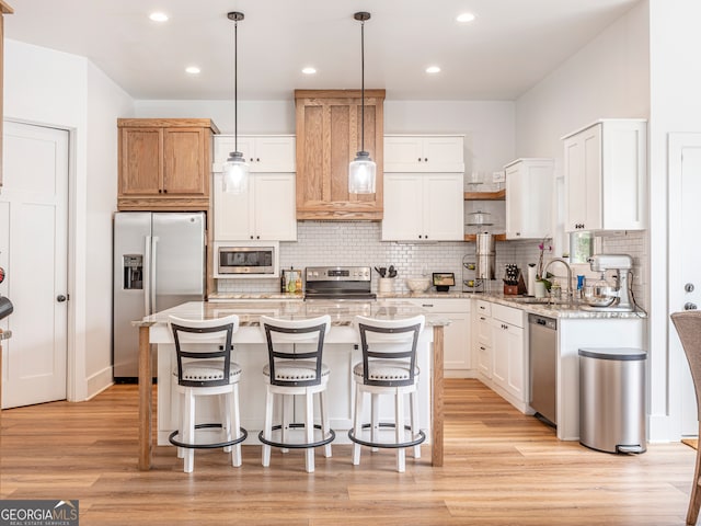 kitchen featuring appliances with stainless steel finishes, a kitchen island, white cabinets, light wood-type flooring, and pendant lighting