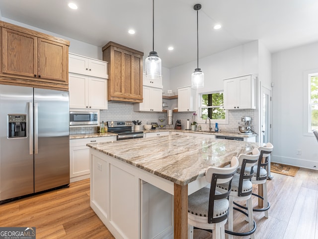 kitchen with decorative light fixtures, stainless steel appliances, white cabinets, a center island, and light wood-type flooring