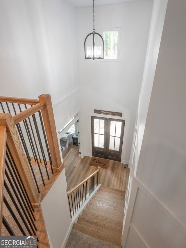 staircase featuring french doors, a chandelier, hardwood / wood-style flooring, and a high ceiling